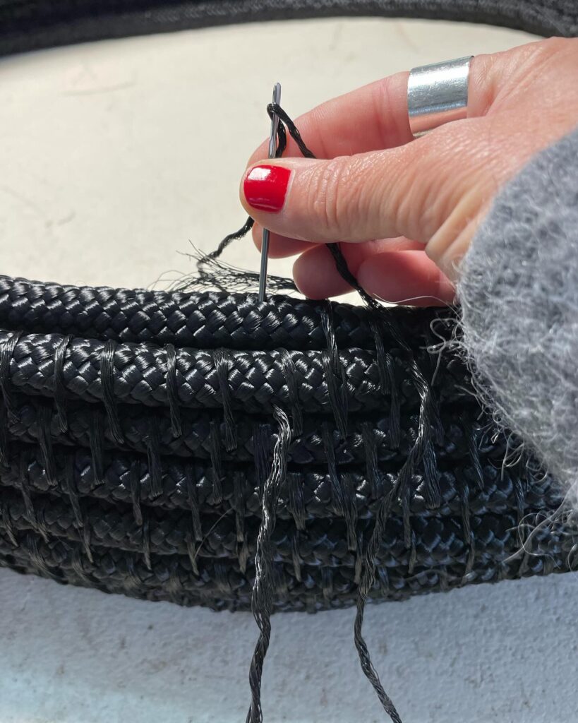 Processo artesanal de escultura têxtil com fios pretos e cordas entrançadas, destacando a precisão do trabalho manual.