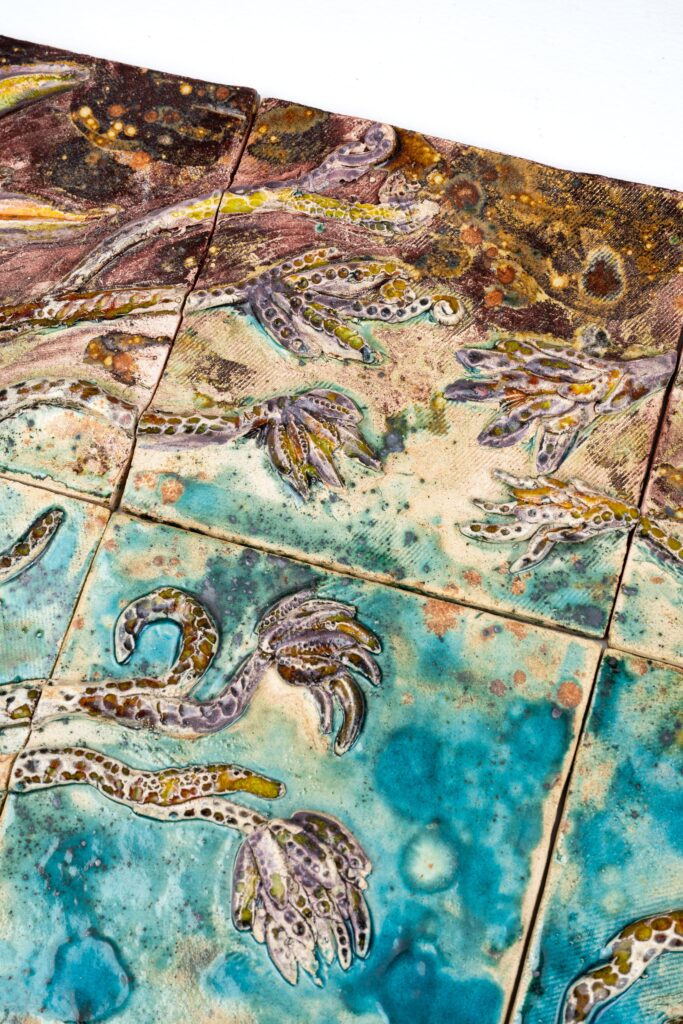 Detalhe da parte inferior do painel cerâmico “O Jardim de Hécate”, com formas botânicas esculpidas e esmaltadas manualmente.